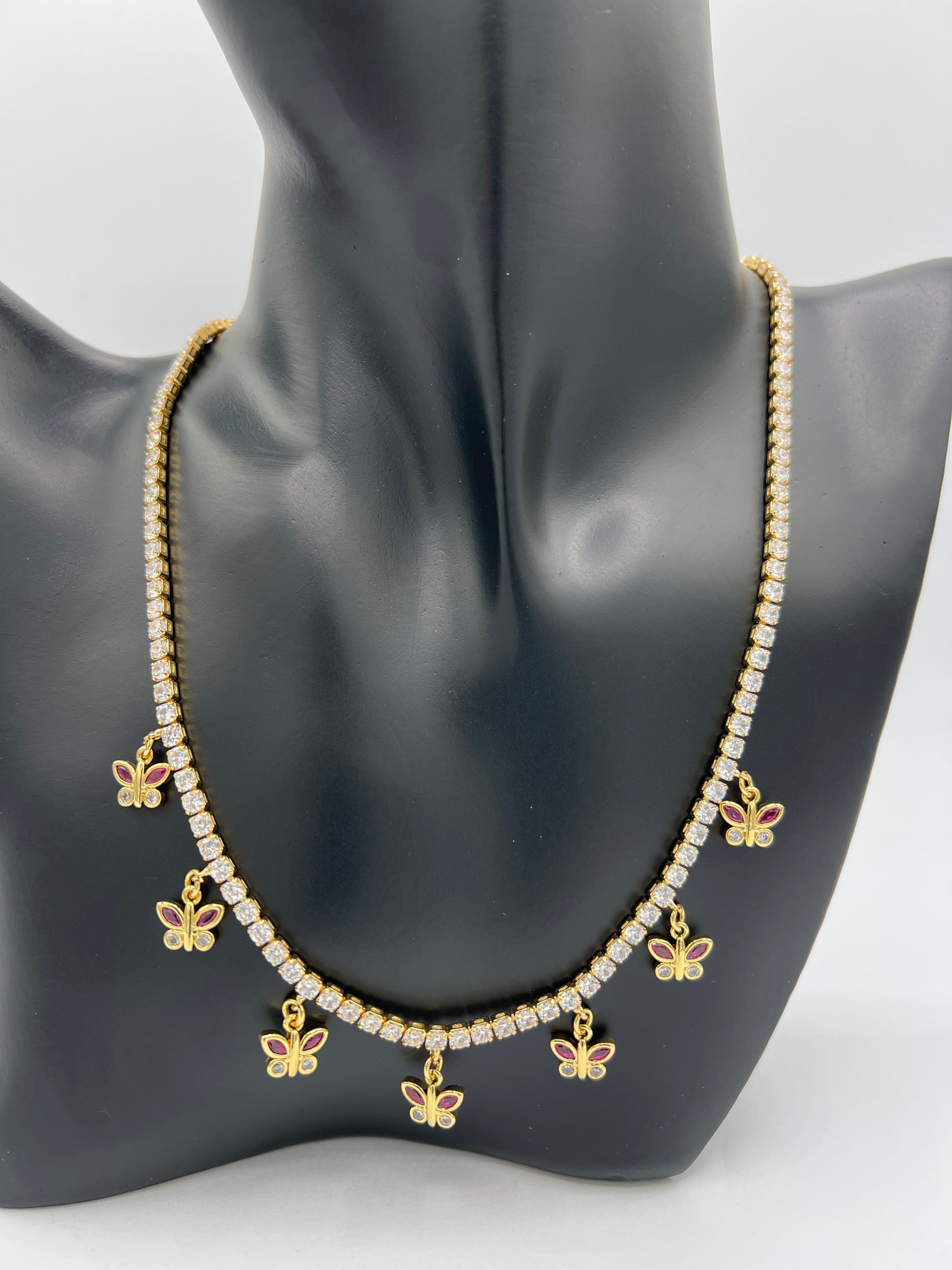 yellow gold plated tennis necklace with butterfly charms hanging the butterfly wings are ruby red and white